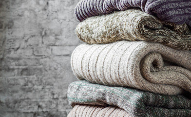 Stack of cozy knitted sweaters on gray wall background