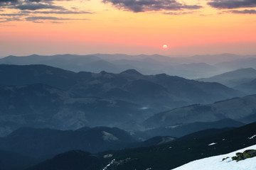 Fototapeta premium From the snow covered meadow opens a panoramic view of the mountains, illuminated by the morning sun rays. Sunrise. Sky with clouds.