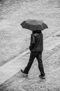 portrait of man walking with umbrella on cobbles place