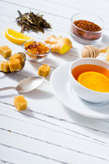 cup of tea, different leaves, honey, lemon ginger and brown sugar on white wooden table background