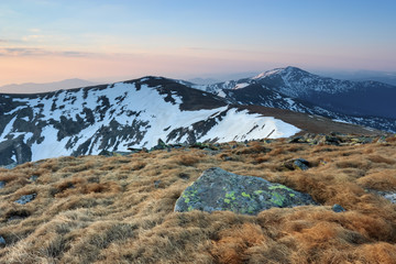 From the lawn opens a panoramic view of the mountains with snow covered picks, illuminated by the morning sun rays. Sunrise.
