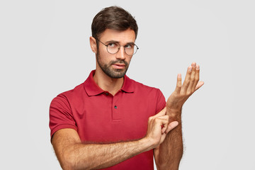 Photo of attractive man wears round spectacles, keeps hand on wrist, checks pulse or heart rate,...