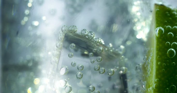 Close-up of a refreshing drink with bubbles interacting with ice and lime.