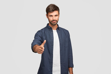 Isolated shot of serious European man makes greeting gesture stretches hand, meets with colleague,...