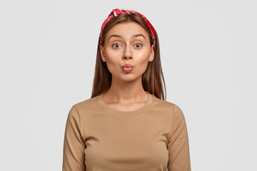 Photo of attractive Caucasian woman round lips, makes grimace, wants to kiss someone, wears...