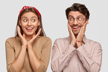 Image of happy two woman and man look joyfully at each other, keep hands on cheeks, express...