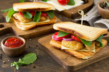 Sandwich with Tomatoes, Cheese, Crispy Chicken Nuggets and Arugula.  Delicious fresh homemade club sandwich with chicken on a wooden table. Fast food.