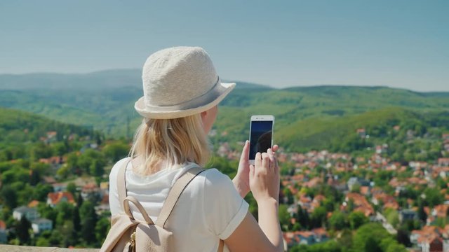 A woman is holding a smartphone in her hands, photographing a beautiful view of a small German town. Holidays and travel in Europe