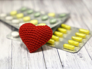 Medical pills and red knitted heart on light wooden table, selective focus. Concept for health...