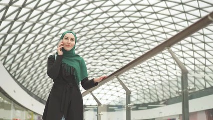 Pretty muslim woman in a hijab with a backpack goes to the shopping center and talks on the phone