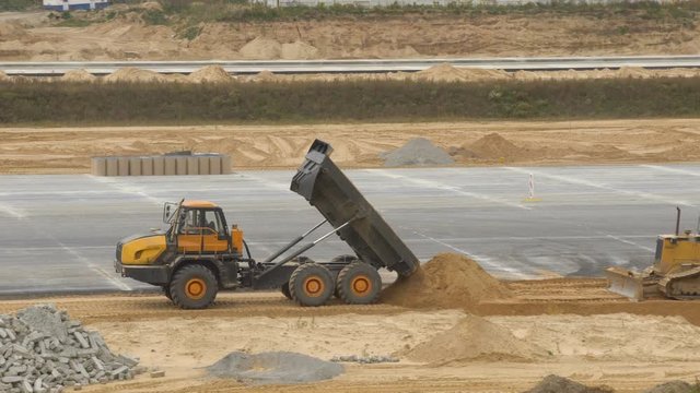 Large quarry dump truck rides, tipper unloads sand on construction site. Concreting of airport runways roads, highway. Machinery works on runway construction of national airport Minsk, MSQ