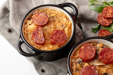 Slovak Christmas cabbage soup in two small pots with sausage on the top on white background.