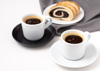 White cups of coffee on black saucer pad with poppy seed cake in behind.