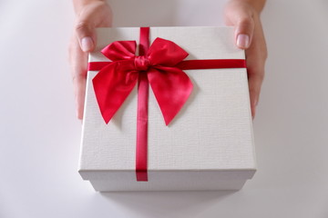 Close-up women hands sending white gift box with red ribbon on white background.