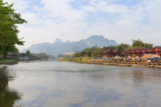 Nam Song River and waterfront restaurant, bungalows and buildings in Vang Vieng, Vientiane Province, Laos, on a sunny day.