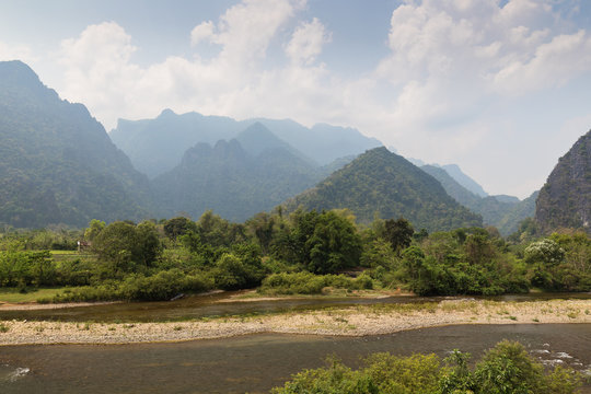 Scenic view of the Nam Song River at low tide and limestone mountains near Vang Vieng, Vientiane Province, Laos, on a sunny day.
