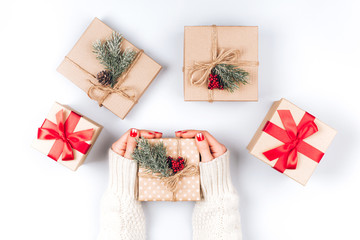 Woman's hands and five vintage minimalistic Christmas gift boxes, decorated with pine cones, pine branches and red berries
