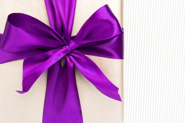 Vertical gift with violet ribbon and bow-knot on light background. Copy space.