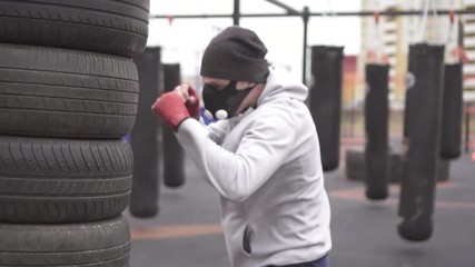 Man athlete in a training mask and boxing types boxing on the street training ground,slow mo