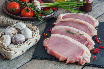 Pieces of grilled pork on a slate with rosemary, garlic in a wicker basket, tomatoes in a rustic style