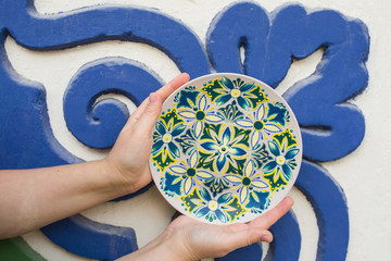 in the hands of a decorative plate on a background of blue-green wall, decorative plate with blue, green flowers, painted plates,