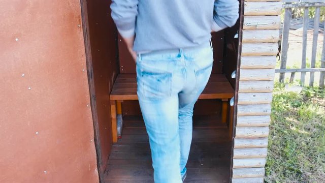 Man pees in outside toilet with a pot in village.