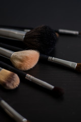 Makeup brushes on dark background spread out by fan, professional makeup brushes, makeup brushes set on black background (vertically; close up; for copy space, text, warm toned)