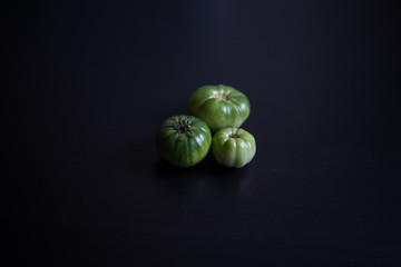 three natural green tomatoes on a dark background (toned for copy space, with empty place)