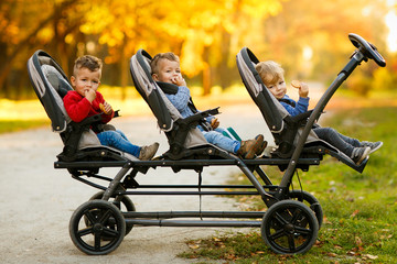 Szczęśliwe trojaczki siedzą w wózku dziecięcym i jedzą ciasteczka na poziomie jesieni - 230132379