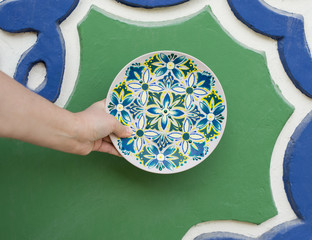 decorative plate on the background of blue-green wall, decorative plate with blue, green flowers, painted plates,