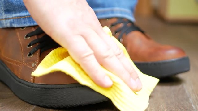 Hand dusting brown leather shoes with a yellow rag from dust and dirt
