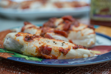  Cooked chicken breasts close up on a plate with cooked tomatoes and fresh herbs topping