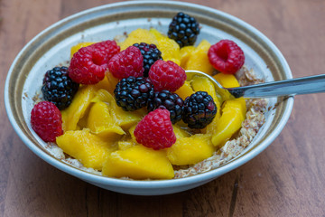 Fresh fruits, peaches, raspberries and blackberries in a bowl over oatmeal as a healthy breakfast