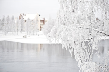 Winter scenery with frost covered trees and old building on riverbank. Selective focus and shallow depth of field.