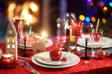 Beautiful table setting for Christmas party or New Year celebration at home. Cozy room with a fireplace and Christmas tree in a background.