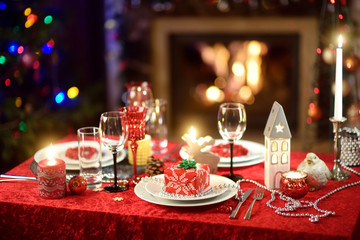 Beautiful table setting for Christmas party or New Year celebration at home. Cozy room with a fireplace and Christmas tree in a background.