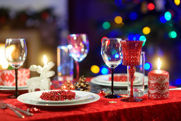 Beautiful table setting for Christmas party or New Year celebration at home. Cozy room with a fireplace and Christmas tree in a background.