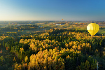 Colorful hot air balloon flying over forest surrounding Vilnius city on sunny autumn evening.