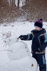 child sculpts snowman,  child for a walk