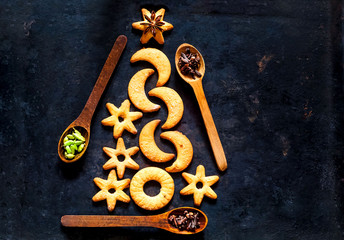 Christmas tree made from cookies and wooden spoons with spices on black background. The concept of celebration and cooking. New Year and Christmas card. Copy space, closeup, top view
