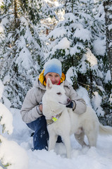 Joyful woman with a white dog in the winter snow-covered forest