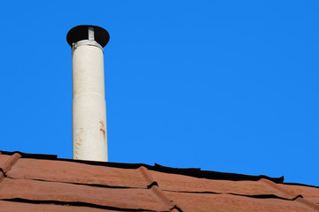 Old chimney of asbestos pipe over a rusty metal roof