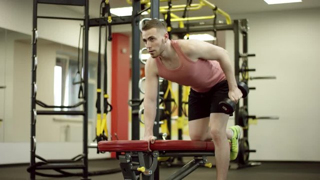 Strong man doing triceps kickbacks exercises with dumbbell in gym