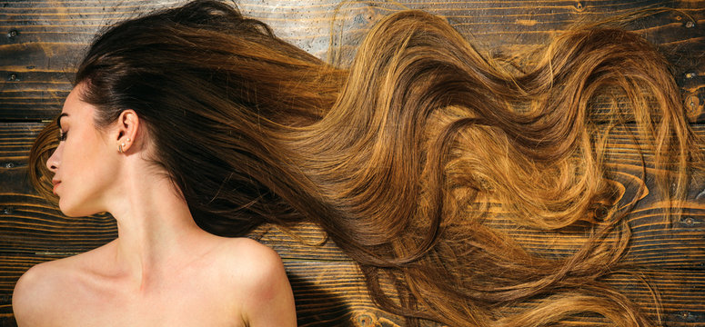 Very Long Hair On Wooden Background. Beautiful Model With Curly Hairstyle. Hair Salon Concept. Care And Hair Products.