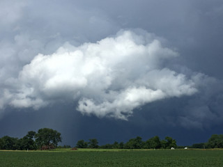 Black thunderstorm passing through farmland with large white cloud