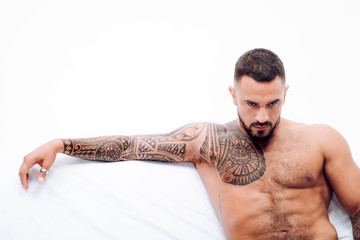Nude male model lies in white bed. Muscular tattooed Man ready to St Valentine's Day. Muscular man...
