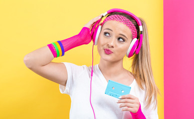 Woman in 1980's fashion holding a cassette tape on a split yellow and pink background