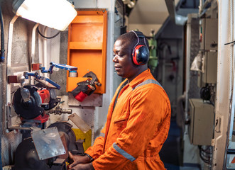 African marine engineer officer in engine control room ECR. He works in workshop with equipment