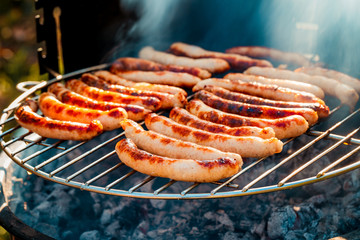 BBQ with fiery sausages on the grill outdoor picnic. Spending time together with the family at the grill. Social meetings, friends. Juicy and well-grilled sausages