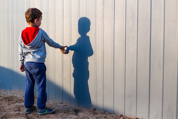boy and his shadow. Lonely little child playing with his shadow outside. imaginary friend. the concept of autism and loneliness. Copy space for your text - obrazy, fototapety, plakaty